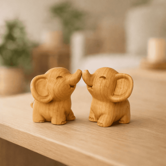 Zwei kleine, handgeschnitzte Elefantenfiguren aus hellem Holz, die sich mit den Rüsseln berühren und lächeln.